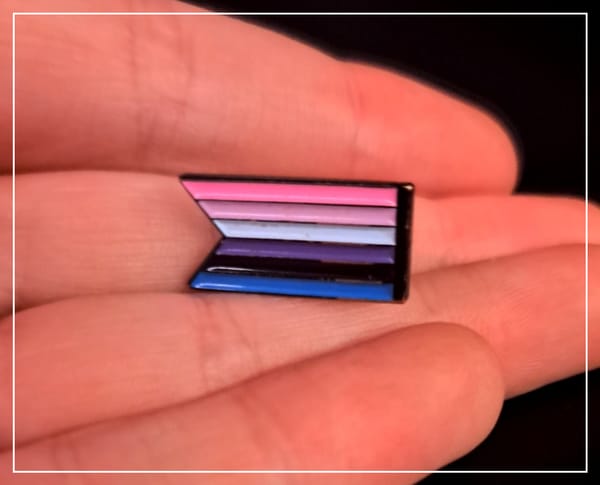 A banner-style enamel pin of the genderfluid pride flag sitting in the hand of the author.